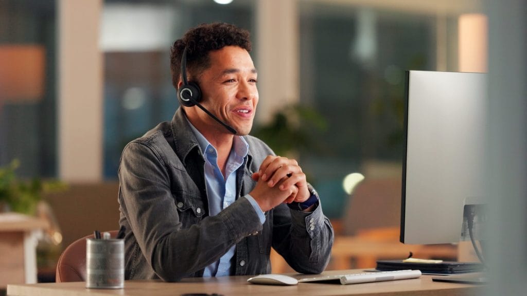 Perfect Plastic Printing team member sitting at desk in front of a computer with a headset assisting a customer with card program solutions.